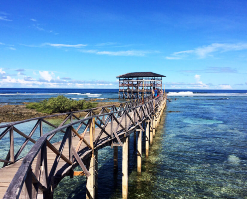 A scenic view of the Cloud 9 Boardwalk in Siargao, stretching over turquoise waters towards the famous surfing waves, with surfers and visitors enjoying the tropical paradise.