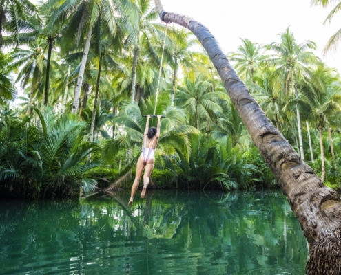 A traveler in mid-air after jumping off the rope swing at Maasin River, with the lush green backdrop of the riverbank.