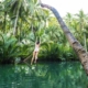 A traveler in mid-air after jumping off the rope swing at Maasin River, with the lush green backdrop of the riverbank.